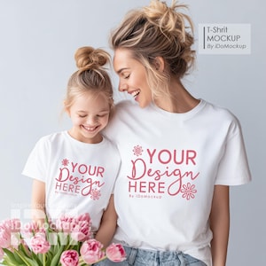 Op de afbeelding: Twee witte t-shirts met de roze tekst "YOUR Design HERE", gedragen door een vrouw en een kind. De vrouw en het kind lachen. De afbeelding bevat een boeket roze bloemen.
