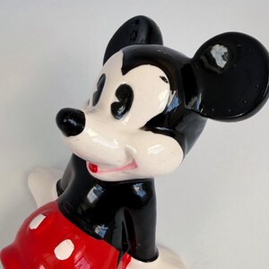 Puede incluir: Una figura de cer&aacute;mica de Mickey Mouse. Tiene un cuerpo, orejas y nariz negros, con una cara blanca y pantalones cortos rojos con botones blancos. La figura tiene un acabado brillante y un dise&ntilde;o de dibujos animados cl&aacute;sico.