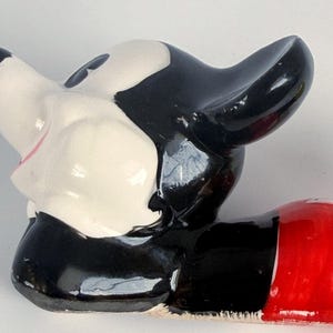 Puede incluir: Una figura vintage de Mickey Mouse, con una cabeza brillante en blanco y negro y un cuerpo inferior rojo. La cara de la figura es blanca con ojos negros y una boca rosa. Las ic&oacute;nicas orejas son prominentes, y el dise&ntilde;o es de estilo de dibujos animados cl&aacute;sico.