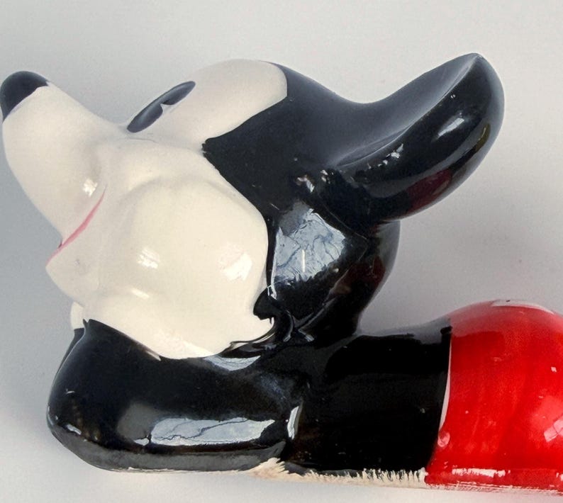 Puede incluir: Una figura vintage de Mickey Mouse, con una cabeza brillante en blanco y negro y un cuerpo inferior rojo. La cara de la figura es blanca con ojos negros y una boca rosa. Las ic&oacute;nicas orejas son prominentes, y el dise&ntilde;o es de estilo de dibujos animados cl&aacute;sico.