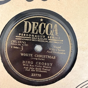 May include: A black Decca Personality Series vinyl record label featuring the text White Christmas by Bing Crosby with Ken Darby Singers and John Scott Trotter and His Orchestra. The label includes the catalog number 23778 and album details.