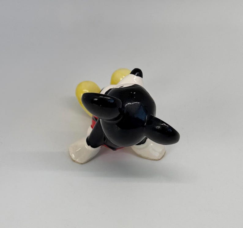 Puede incluir: Una figura de cer&aacute;mica de Mickey Mouse, vista desde arriba. La figura tiene cabeza y orejas negras, cara blanca y un atuendo rojo y blanco. Se ven las manos amarillas de la figura.