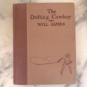 May include: A hardcover book titled The Drifting Cowboy by Will James with a tan cover and a dark brown spine. The front cover features a dark brown line drawing of a cowboy swinging a lasso. The text is printed in a dark brown serif font.