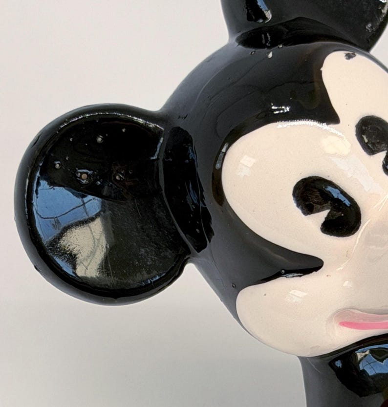 Puede incluir: Primer plano de una figura de cer&aacute;mica de Mickey Mouse en blanco y negro. La figura tiene un acabado brillante, con orejas, ojos y nariz negros. La cara es blanca con ojos negros y boca rosa. La figura es un personaje de dibujos animados cl&aacute;sico.