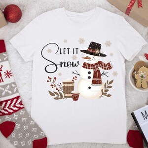 May include: White t-shirt with a snowman graphic and the text "Let it snow". The snowman is wearing a red and black plaid scarf and a black hat.