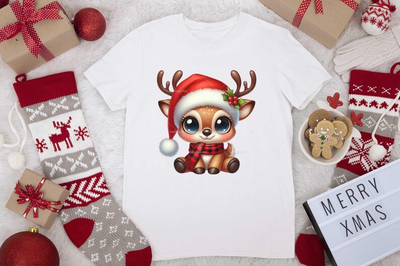 Op de afbeelding: Wit T-shirt met een cartoon afbeelding van een rendier dat een rode kerstmanmuts en een rood-zwarte sjaal draagt. Het rendier heeft grote blauwe ogen en een bruine neus.