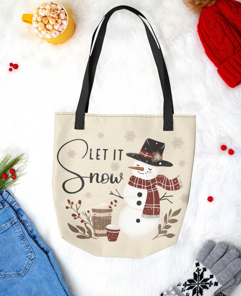 May include: A beige tote bag with black straps features a snowman wearing a red and black plaid scarf and a black hat with a red flower. The bag has the text "Let it Snow" in black script.