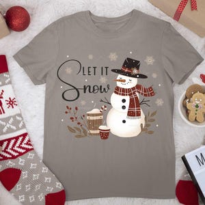 May include: A gray t-shirt with a snowman graphic and the text "Let it snow". The snowman is wearing a red and black plaid scarf and a black hat. There are snowflakes and brown branches around the snowman.