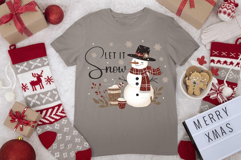May include: A gray t-shirt with a snowman graphic and the text "Let it snow". The snowman is wearing a red and black plaid scarf and a black hat. There are snowflakes and brown branches around the snowman.
