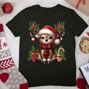 Pode incluir: Camiseta preta com uma rena de desenho animado usando uma echarpe xadrez vermelha e preta e um chap&eacute;u de Papai Noel. A rena est&aacute; cercada por luzes de Natal, presentes e bengalas de doces.