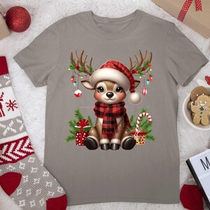Pode incluir: Uma camiseta cinza com uma rena de desenho animado usando um chap&eacute;u de Papai Noel vermelho e branco e uma echarpe xadrez vermelha e preta. A rena est&aacute; cercada por luzes de Natal, presentes e bengalas de doces.