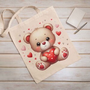 May include: A beige tote bag with a cartoon illustration of a brown teddy bear holding a red heart. The background is filled with small red and gray hearts.