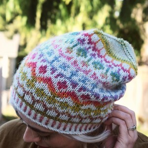 May include: A colorful knitted beanie hat with a geometric pattern. The hat features a mix of colors including white, pink, blue, yellow, and green. The hat is made of a soft, textured yarn and is designed to be worn on the head.