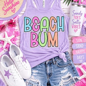 May include: A light purple tank top with the text BEACH BUM in colorful sequin letters, paired with distressed blue denim shorts, white sneakers with purple glitter stars, a straw hat with Hello Sunshine text, and a white tumbler with Sandy Toes Salty Vibes text.