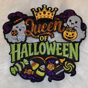 May include: A sequined Halloween decoration with the words "Queen of Halloween". The design features a gold crown, two smiling ghost characters, and various candies. The text and design elements are outlined in sequins.
