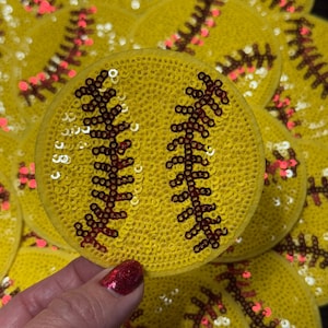 Pode incluir: Remendos de softball amarelos com lantejoulas e detalhes de costura vermelha. Os remendos s&atilde;o redondos e apresentam o design cl&aacute;ssico de softball. A imagem mostra uma cole&ccedil;&atilde;o desses remendos, com um sendo segurado na m&atilde;o.