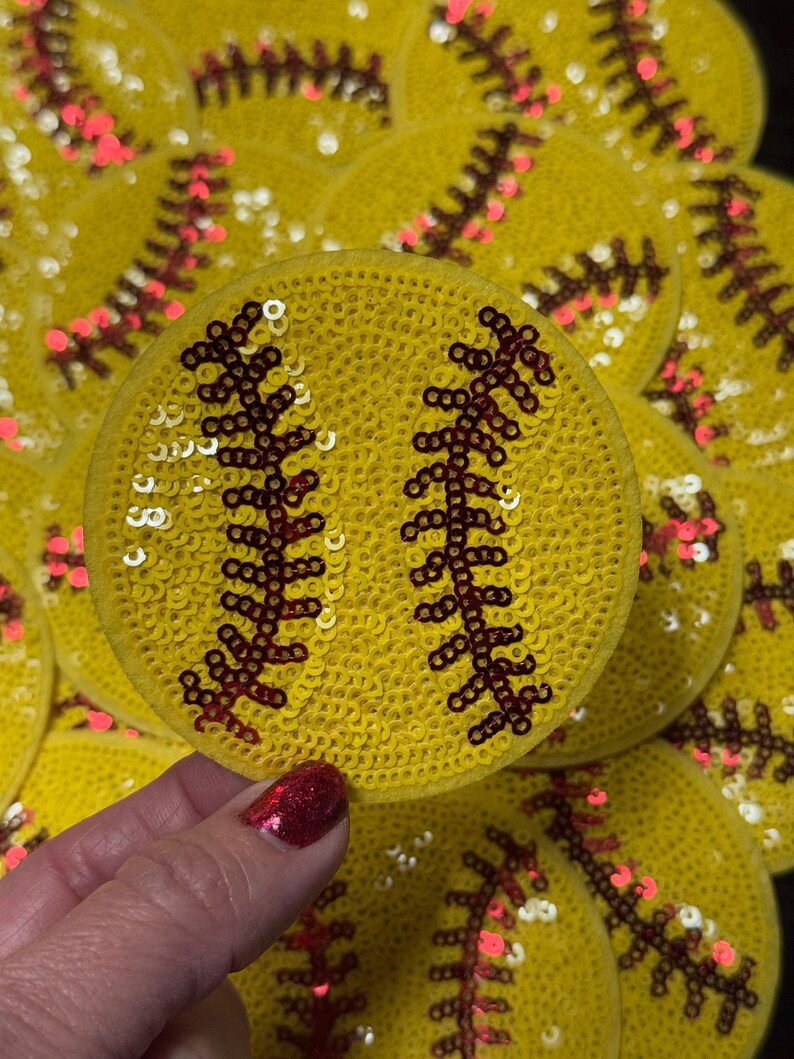 Pode incluir: Remendos de softball amarelos com lantejoulas e detalhes de costura vermelha. Os remendos s&atilde;o redondos e apresentam o design cl&aacute;ssico de softball. A imagem mostra uma cole&ccedil;&atilde;o desses remendos, com um sendo segurado na m&atilde;o.