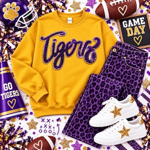 May include: A gold crewneck sweatshirt with the word Tigers in purple sequins, purple and black leopard print jeans, and white sneakers with gold glitter stars. The outfit is surrounded by a football helmet, a megaphone, and a sign reading GAME DAY.