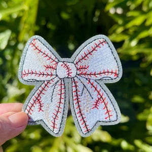 May include: A white bow with red stitching, resembling a baseball, with a glittery background.