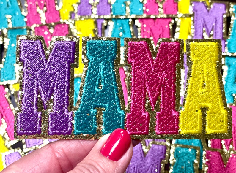 Peut inclure: Un ensemble de quatre lettres en feutre color&eacute; &eacute;pellant "MAMA" avec une bordure dor&eacute;e paillet&eacute;e. Les lettres sont brod&eacute;es et ont une texture l&eacute;g&egrave;rement en relief.