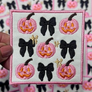 May include: Embroidered patch featuring pink jack-o'-lanterns with orange grins, black bows, and gold starbursts on a white background. The patch has a pink border. The design is repeated on other patches in the background.