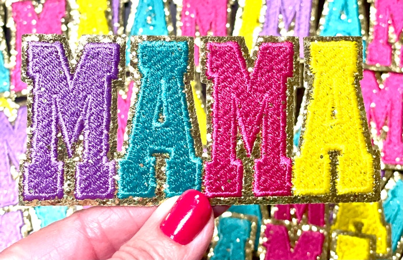 Peut inclure: Un ensemble de cinq lettres en feutre color&eacute; &eacute;pellant "MAMA" avec une bordure dor&eacute;e paillet&eacute;e. Les lettres sont violettes, turquoise, roses et jaunes.