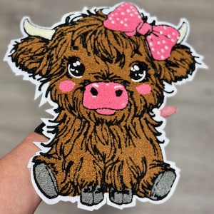 Puede incluir: Un parche bordado de una vaca Highland con un lazo rosa. La vaca es marrón y negra con la nariz rosa y las mejillas rosas. El parche es perfecto para añadir un toque de fantasía a cualquier proyecto.