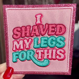 May include: Pink embroidered patch with the text "I SHAVED MY LEGS FOR THIS" in pink and teal. The patch has a glittery pink border and is square-shaped.