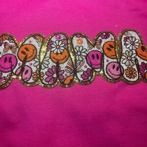 May include: Pink fabric with a gold glitter embroidered patch that says "MAMA" in a retro font with smiley faces and flowers.