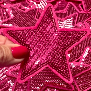 May include: A pile of pink sequined star-shaped patches. The stars are made of a shiny fabric with a pink backing.