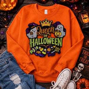 May include: An orange crewneck sweatshirt featuring a central graphic with the text Queen OF HALLOWEEN in gold and green glittery script. The design includes two white ghosts, a gold crown, and colorful candy illustrations with purple accents.