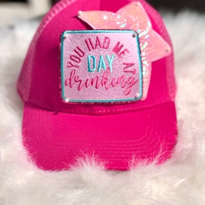 Op de afbeelding: Roze trucker cap met een roze en blauwe patch met de tekst "You had me at day drinking" en een glinsterende roze ster.