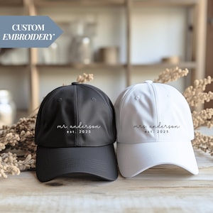 Pode incluir: Duas bonés de beisebol, um preto e um branco, com o texto "mrs. anderson est. 2025" bordado na frente.