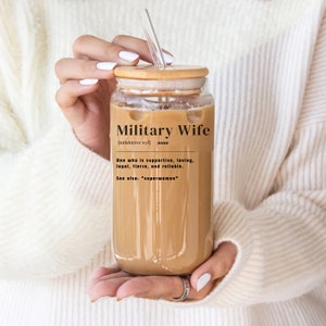 Op de afbeelding: Een glazen beker met een bamboe deksel en een rietje. De beker bevat een bruine vloeistof en een zwart-witte afbeelding met de tekst "Military Wife [milahteree wyf] noun One who is supportive, loving, loyal, fierce, and reliable. See also: "superwoman""