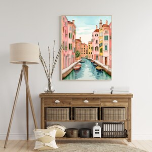May include: A watercolor painting of a canal in Venice, Italy. The canal is lined with colorful buildings, and there are gondolas floating in the water. The painting is framed in a light wood frame.