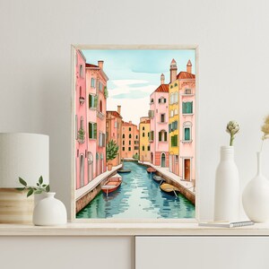 May include: A watercolor painting of a canal in Venice, Italy. The canal is lined with colorful buildings, and there are several gondolas in the water. The painting is framed in a light wood frame.