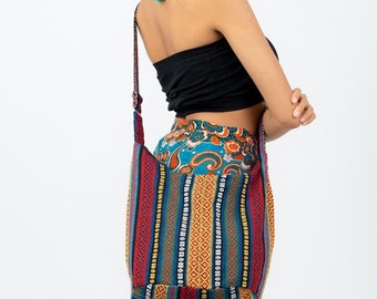 May include: A woman wearing a black top and a long, teal skirt with a colorful paisley pattern. She is carrying a colorful striped tote bag with a long strap over her shoulder.