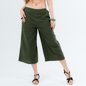 Puede incluir: Top de tubo negro y pantalones culotte verde oliva. Los culottes son de pernera ancha y llegan a la mitad de la pantorrilla. La modelo lleva sandalias negras con detalles dorados. El fondo es blanco liso.