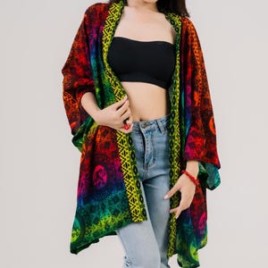 May include: A vibrant, patterned kimono in shades of red, orange, yellow, green, and blue. The kimono features a geometric design and is worn over a black tube top and light blue jeans. A red bracelet is visible on the wrist.