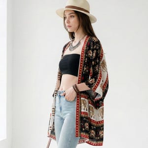 May include: A woman wearing a cream-colored hat with a brown band, a black tube top, light blue jeans, and brown ankle boots. She is also wearing a patterned kimono with elephant designs, a necklace, and a brown leather bag.