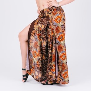 May include: A white crop top paired with brown floral print palazzo pants. The pants feature a high slit on each leg, showcasing a vibrant floral pattern in shades of orange, red, and blue. Black sandals complete the outfit.