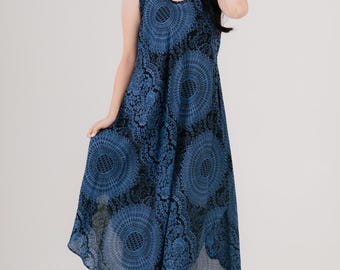 May include: A sleeveless, knee-length blue dress with a circular pattern. The dress has a scoop neckline and a flowing skirt. The model is wearing black sandals and a red bracelet. The dress is made of a lightweight fabric.