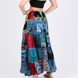 Peut inclure: Longue jupe patchwork avec divers motifs colorés, dont des motifs floraux et éléphants. La jupe est associée à un crop top noir. Le design de la jupe intègre des panneaux rouges, bleus et verts, créant une esthétique bohème.