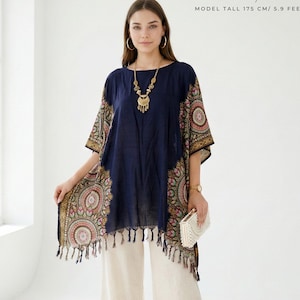 Puede incluir: Una túnica azul marino con paneles estampados y flecos, combinada con pantalones de pierna ancha color crema. La parte superior presenta un collar dorado. La imagen incluye el texto "Home64Studio" y "MODEL TALL 175 CM/ 5.9 FEET".