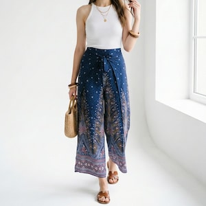 May include: A woman wearing a white ribbed tank top and blue patterned palazzo pants. She is carrying a straw handbag and wearing brown sandals. The pants have a peacock feather design. The model is 5.9 feet tall.