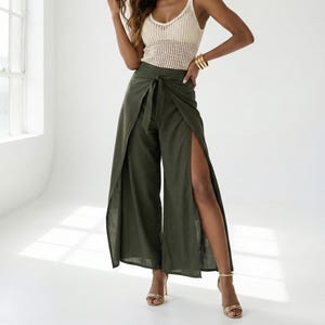 May include: A sleeveless cream-colored crochet tank top with a scoop neckline paired with olive green wide-leg trousers featuring a front tie waist and high side slits. The text Home 64 Studio and Model tall 175 cm/ 5.9 feet is visible.