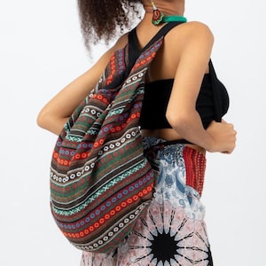 May include: A woman wearing a black top and a colourful patterned skirt is carrying a large, brown, black, red and green patterned drawstring bag.