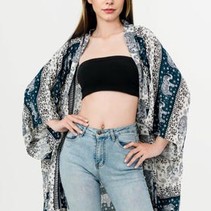 Pu&ograve; includere: Kimono fantasia blu navy, bianco e grigio con motivi a elefante. La modella indossa un top a fascia nero e jeans azzurri. Il kimono &egrave; aperto.