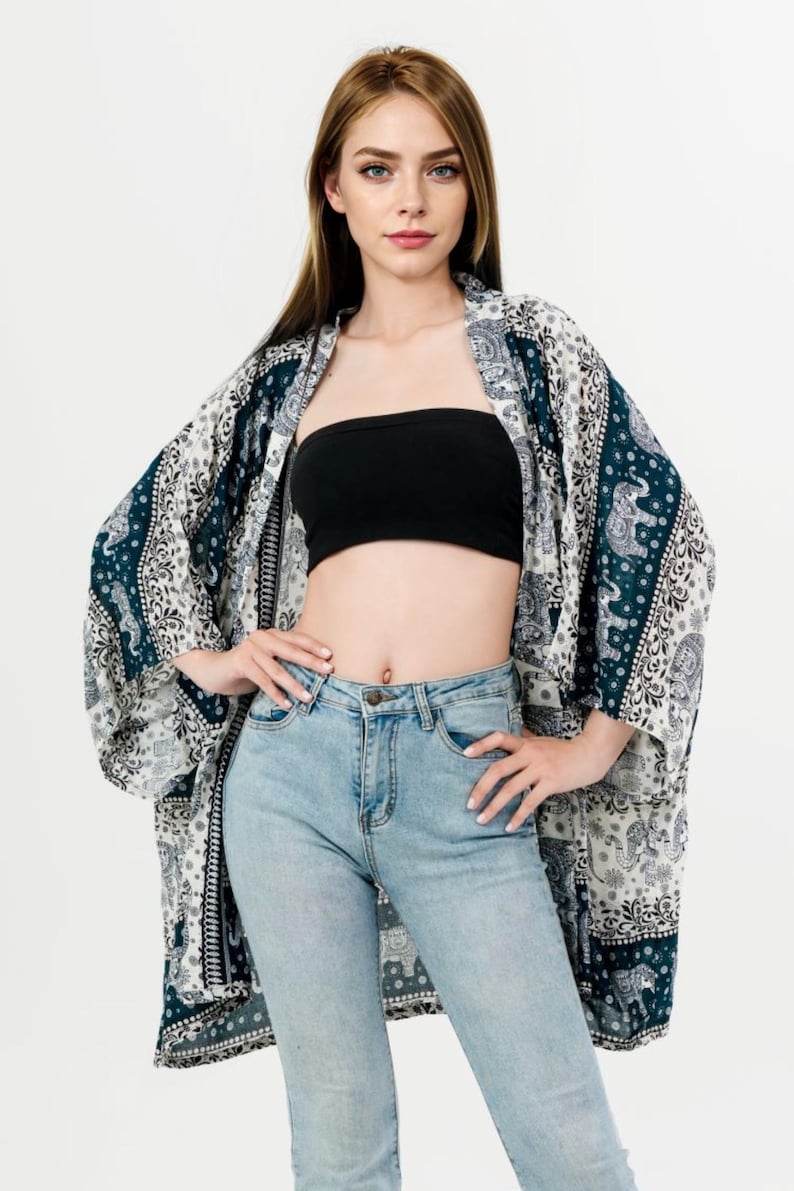 Pu&ograve; includere: Kimono fantasia blu navy, bianco e grigio con motivi a elefante. La modella indossa un top a fascia nero e jeans azzurri. Il kimono &egrave; aperto.