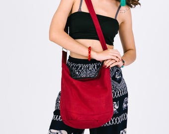 Può includere: Una borsa a tracolla in tela rossa con una tracolla nera. La borsa è indossata da una persona che indossa una canotta nera e pantaloni a fantasia bianco e nero.